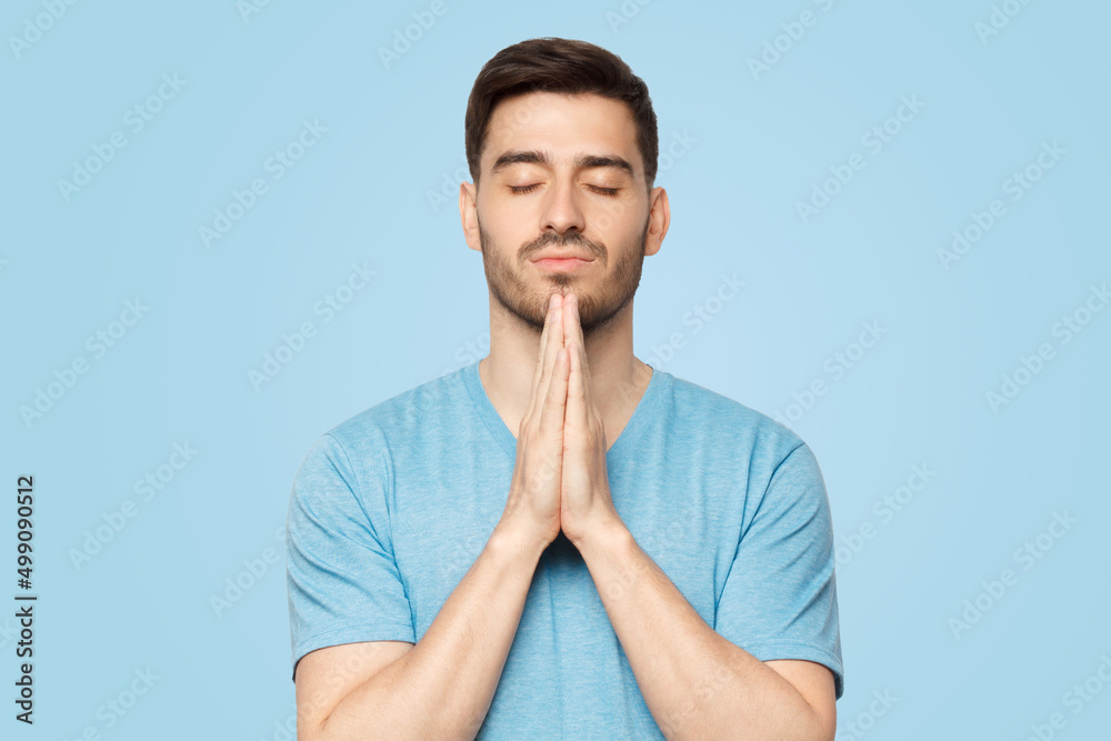 Young man putting hands together as if he is praying with closed eyes Young man putting hands together as if he is praying with closed eyes