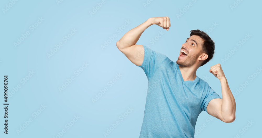 Young successful man in blue tshirt screaming yes and raising clenched fist Young successful man in blue tshirt screaming yes and raising clenched fist