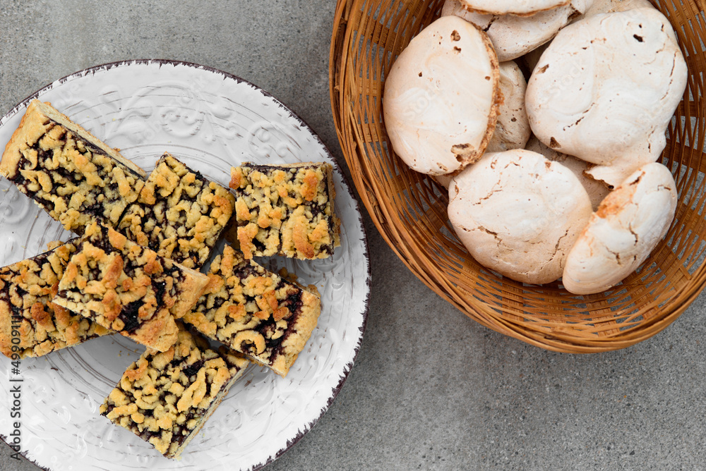 Meringue and cookies on a gray background. The homemade pie is cut into squares and lies on a white plate. Meringue in a rattan basket. Meringue and cookies on a gray background. The homemade pie is cut into squares and lies on a white plate. Meringue in a rattan basket.