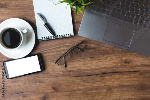 An office desk with a cup of coffee, a mobile phone, glasses, a pen and laptop.Top view mock-up