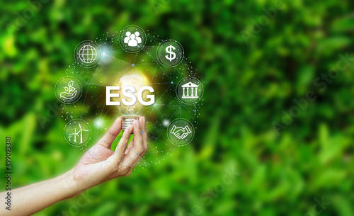 Hand holding light bulb with ESG icon concept for environmental, social, and governance in sustainable and ethical business on the Network connectionon a green nature background. 