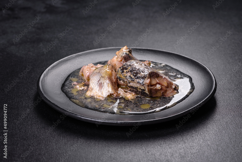Canned sardine in oil on a black round plate against a dark concrete background Canned sardine in oil on a black round plate against a dark concrete background