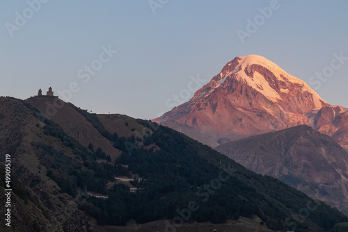 Distant view on Gergeti Trinity Church in Stepansminda, Georgia. The church is located the Greater Caucasian Mountain Range. Clear sky above the snow-capped Mount Kazbegi in the back. Sunrise, sunset