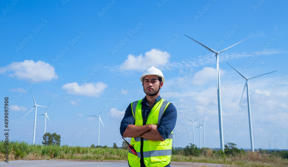 Engineer wearing uniform ,helmet hold document inspection work in wind turbine farms rotation to generate electricity energy. Green ecological power energy generation wind sustainable energy concept. Engineer wearing uniform ,helmet hold document inspection work in wind turbine farms rotation to generate electricity energy. Green ecological power energy generation wind sustainable energy concept.