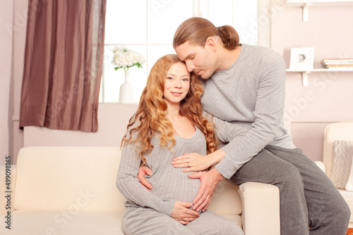 Happy Beautiful Pregnant woman with her husband sitting on sofa at home looking at camera © luengo_ua