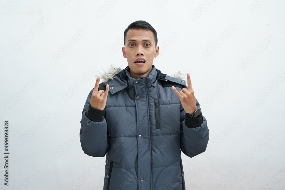 Asian man wearing winter jacket over isolated white background. screaming with a crazy expression doing rock symbols with hands up. Music star. Heavy concept. Asian man wearing winter jacket over isolated white background. screaming with a crazy expression doing rock symbols with hands up. Music star. Heavy concept.