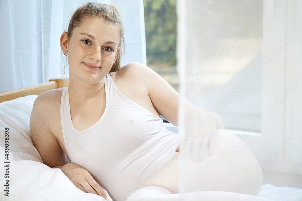 Gorgeous young woman wears white body suit as underwear and lies relaxed on bed