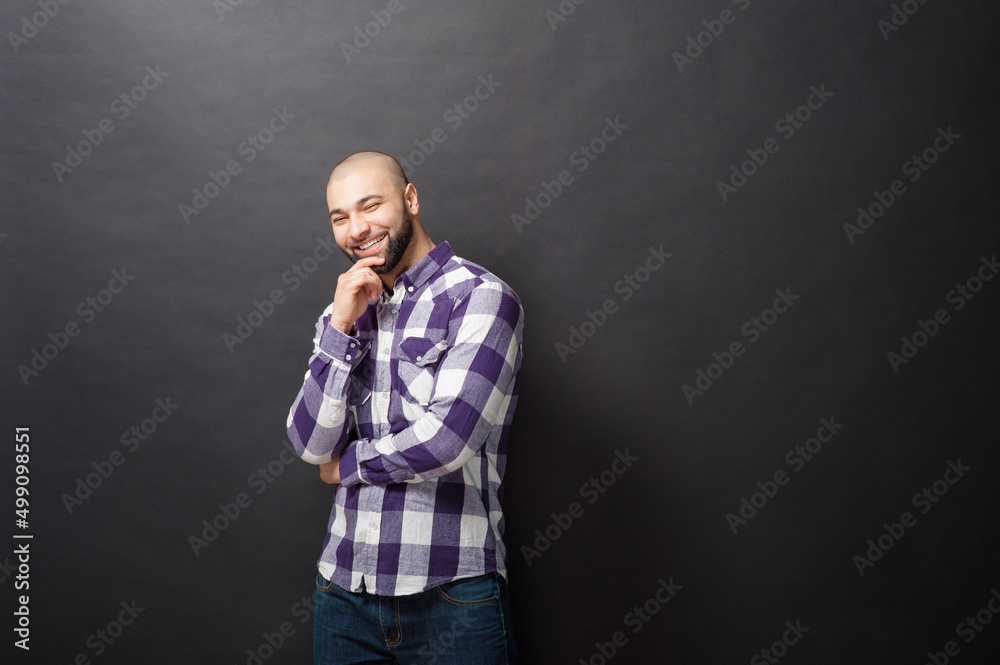Thoughtful handsome. Handsome young smiling man in casual shirt holding hand on chin and looking at camera while standing against black background. Thoughtful handsome. Handsome young smiling man in casual shirt holding hand on chin and looking at camera while standing against black background.