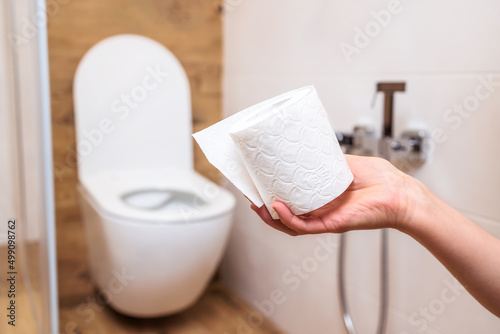 A woman's hand holds a roll of white toilet paper close-up. Bathroom background photo