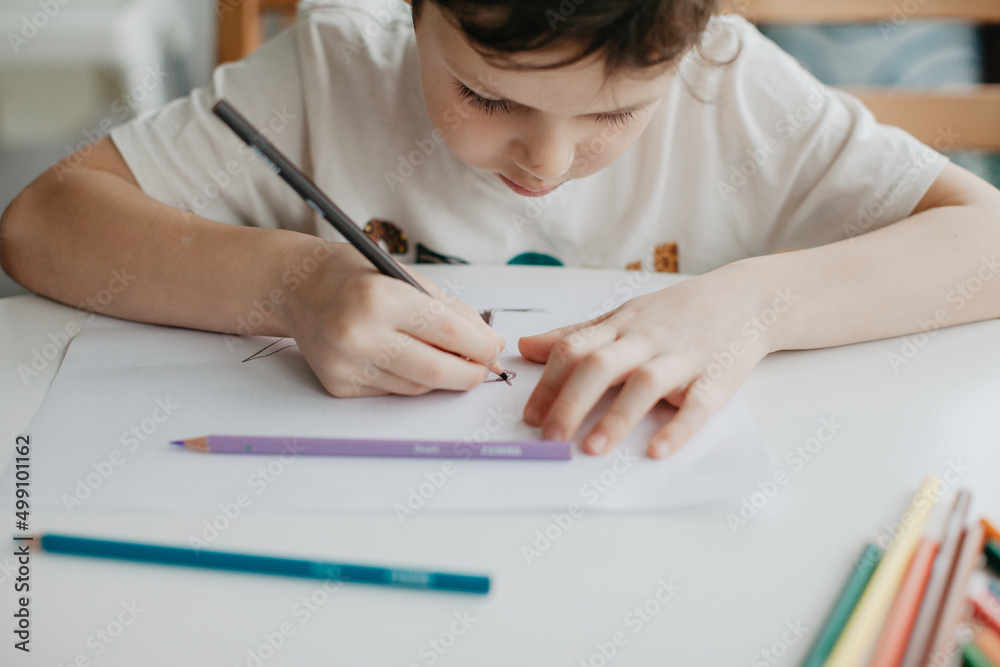The boy draws with pencils at the kitchen