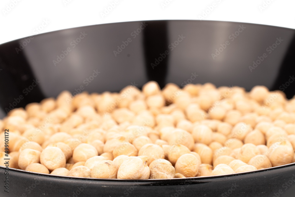 Several uncooked hummus grains in a black ceramic plate, close-up, isolated on white. Several uncooked hummus grains in a black ceramic plate, close-up, isolated on white.
