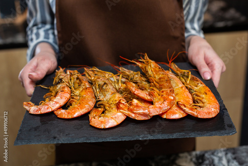 Close-up. A woman in the kitchen holds tiger prawns on a tray.