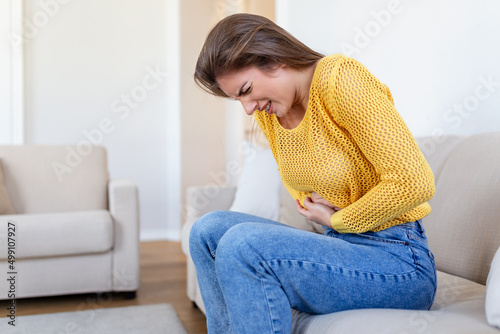 Woman lying on sofa looking sick in the living room. Beautiful young woman lying on bed and holding hands on her stomach. Woman having painful stomachache on bed, Menstrual period photo