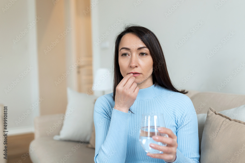 Asian woman takes pill with glass of water in hand. Stressed female drinking sedated antidepressant meds. Woman feels depressed, taking drugs. Medicines at work Asian woman takes pill with glass of water in hand. Stressed female drinking sedated antidepressant meds. Woman feels depressed, taking drugs. Medicines at work
