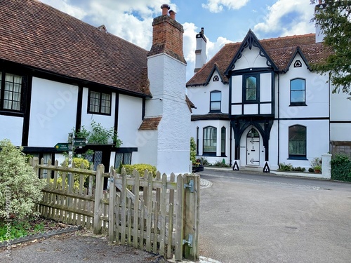 Cookham village, England, Berkshire. Church gate street view. Old half timbered house opposite Holy Trinity church in medieval village White facade with black beams red tile roof chimney old lantern photo