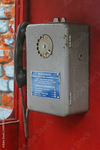 Old soviet telephone with a warning table about the surcharge for a long call and with emergency phone numbers (written in Russian) hanging in booth