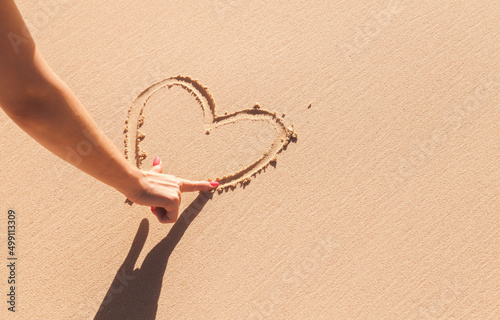 Girls hand drawing a heart sign on wet coastal sand