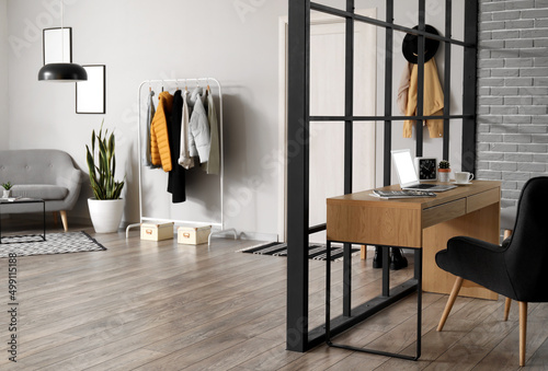 Interior of stylish room with workplace and hanger with jackets © Pixel-Shot
