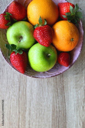 Pink bowl filled with fresh apples  oranges and strawberries on wooden table. Flat lay.