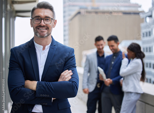 Confident with a great team behind me. Cropped portrait of a handsome mature businessman standing outside with his arms folded with his colleagues in the background. photo