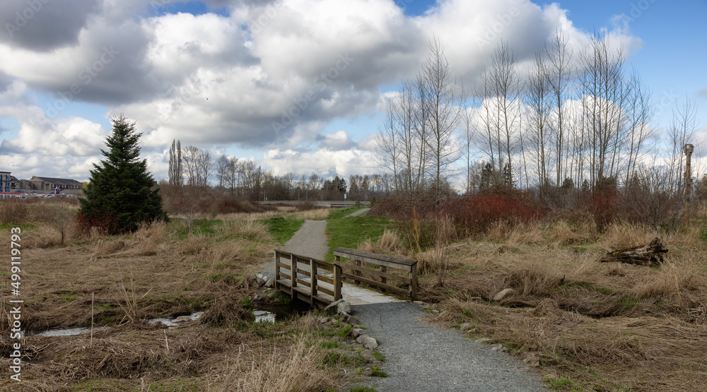 Scenic path in a park with green field and trees in a city. Sunny Sky with clouds. Derek Doubleday Arboretum, Langley, Vancouver, BC, Canada. Scenic path in a park with green field and trees in a city. Sunny Sky with clouds. Derek Doubleday Arboretum, Langley, Vancouver, BC, Canada.