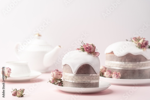 Glazed Easter cakes decorated with dry tea rose flowers on pastel pink background. Easter composition with cakes, roses and chocolate eggs. Holiday background with copy space for your design.