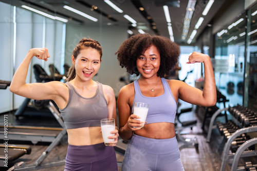 Asian and African American woman finishing workout and drinking protein milk shake vitamins after training. Bodybuilding. Healthy Friend lifestyle. © anon