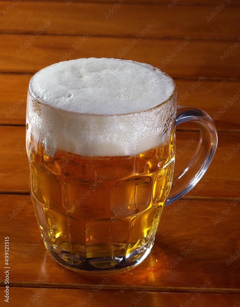 One glass mug with lager or porter is delicious frothy beer on a wooden tabletop a sunny day.