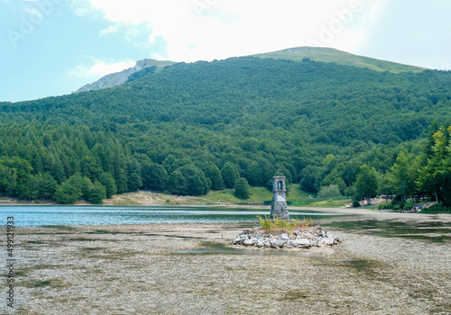 lake Calamone and a monument on it across the mountain Ventasso on a sunny day. Water reflections. Landscape background. National park of Appennino Tosco-Emiliano 