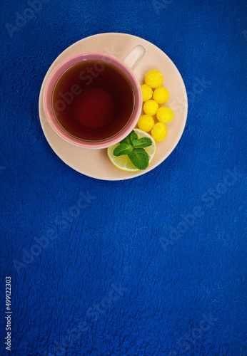cup of tea with lemon, mint and sweets on a blue background. vertical frame