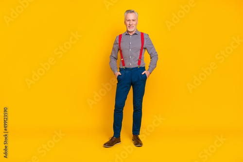 Full length body size view of attractive cheerful middle-aged man holding hands in pockets isolated over bright yellow color background