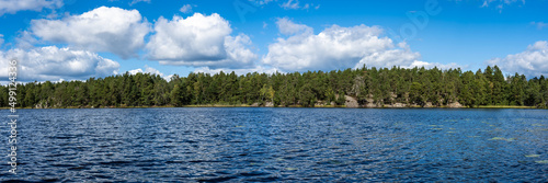 Amazing view of forest shores blue water lake. Scandinavian landscape. Panoramic view Swedish scenery in autumn sunny day. Rocky islands covered with various coniferous trees pines. Banner. Header.