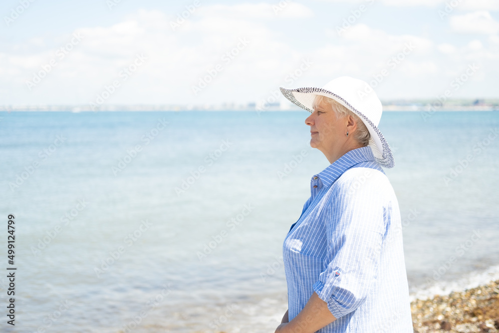 portrait of happy senior woman in straw hat and blue shirt staying on seaside