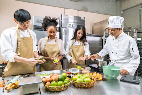Obraz na plátne Cooking  course , senior Asian male chef in cook uniform teaches young asian and african american people cooking class students to prepare, mix ingredients for  foods, fruit pies in   kitchen