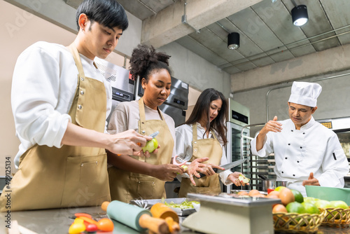 Cooking  course , senior Asian male chef in cook uniform teaches young asian and african american people cooking class students to prepare, mix ingredients for  foods, fruit pies in   kitchen. photo