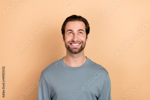 Photo of young cheerful man curious interested look empty space thoughtful minded isolated over beige color background