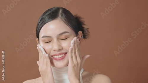 A young woman with beautiful face smiling, washing her face over brown background , beauty skin care concept