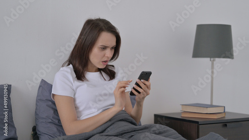 Woman Reacting to Loss on Smartphone in Bed