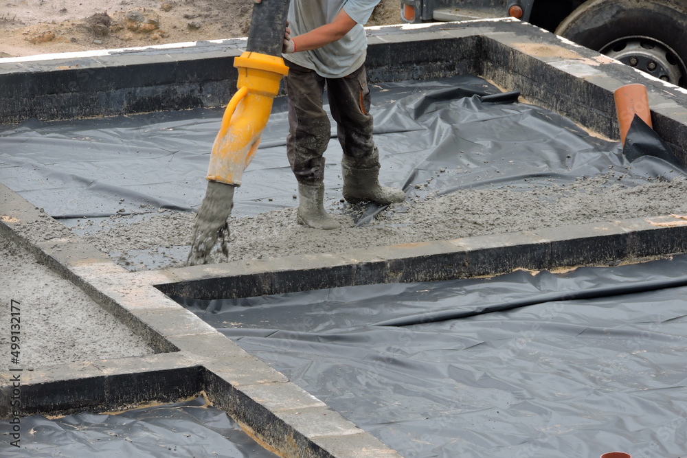 A building worker pouring a concrete slab foundation using a hose of a