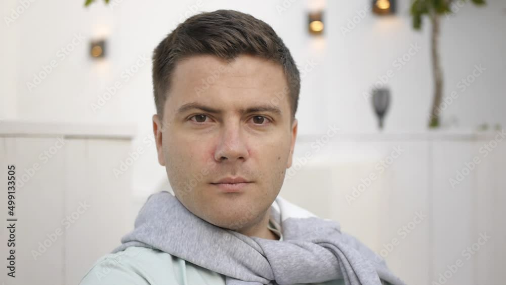 Close up of confident handsome man wearing casual clothes looking at camera on blurred white terrace background Close up of confident handsome man wearing casual clothes looking at camera on blurred white terrace background