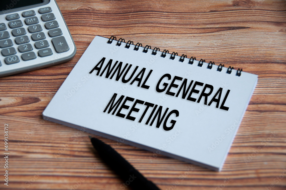 Annual general meeting text on notepad with calculator, pen and wooden table background. Annual general meeting text on notepad with calculator, pen and wooden table background.