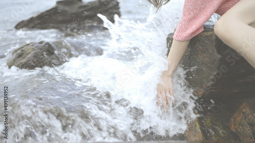 Girl sitting on the rocks. Young woman's hand touching the water in the sea, catching the wave with her hand. Splashing Waves at Blowing Rocks.