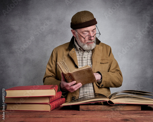 Slika na platnu casual studio portrait of a bearded senior man reading and browsing old books