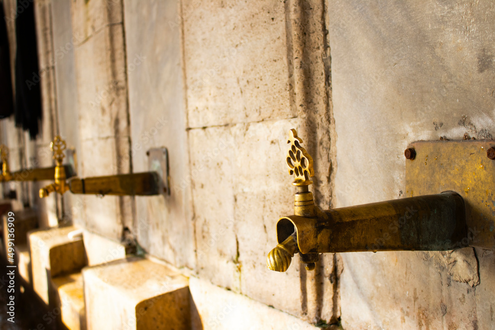 Selective ablution place for Muslims in Istanbul. Fountain made of yellow brass, on blurred limestone wall. Selective ablution place for Muslims in Istanbul. Fountain made of yellow brass, on blurred limestone wall.