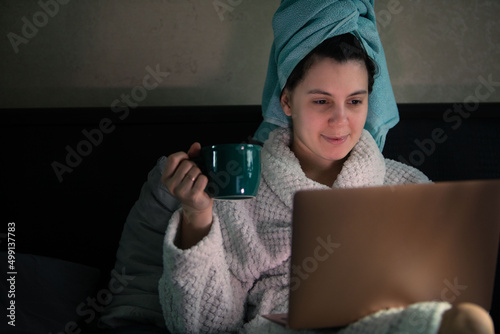 woman laying down in bed with wet head covered with towel working on laptop