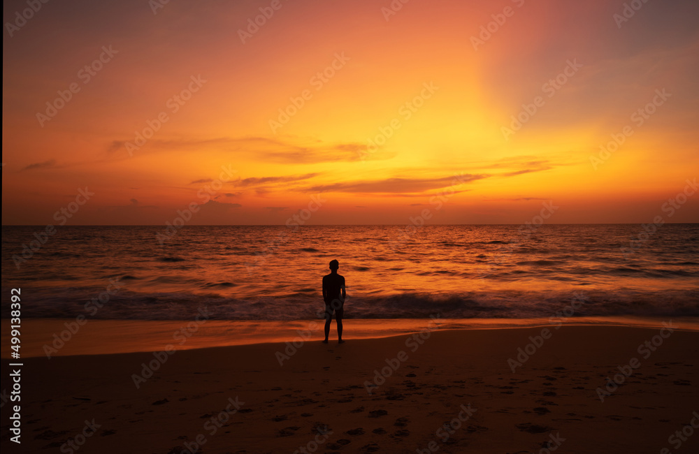 A man standing on the beach looking at sunset sky at Naithon beach, Phuket, Thailand.