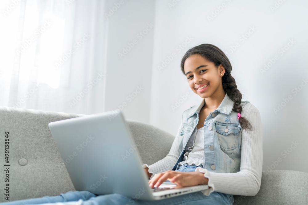 African Teen Girl Using Laptop Computer Browsing Internet Sitting On Couch At Home African Teen Girl Using Laptop Computer Browsing Internet Sitting On Couch At Home