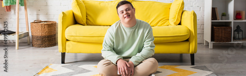 Happy teenager with down syndrome sitting on floor at home, banner. photo