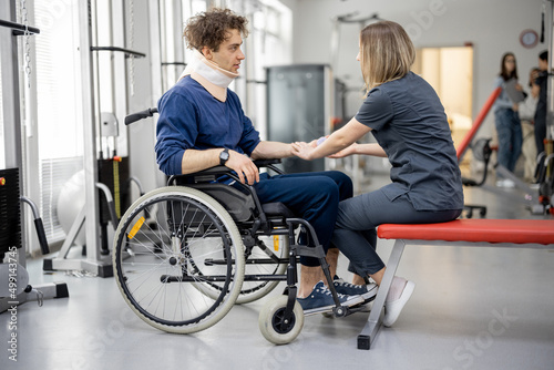 Rehabilitation specialist helps a guy to do exercises for recovery from injury, who is sitting in a wheelchair with a corset around his neck. Concept of physical therapy for people with disabilities © rh2010