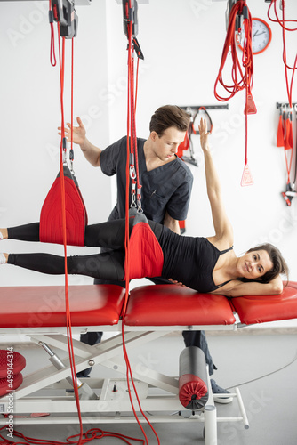 Rehabilitation specialist doing active treatment on suspension straps to female patient. Concept of therapeutic exercises to restore pain-free movement patterns and improve function photo